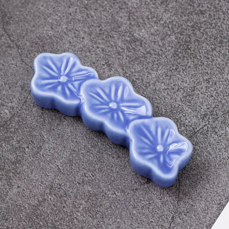 Three blue ceramic flower-shaped kawaii chopstick holder on a gray surface