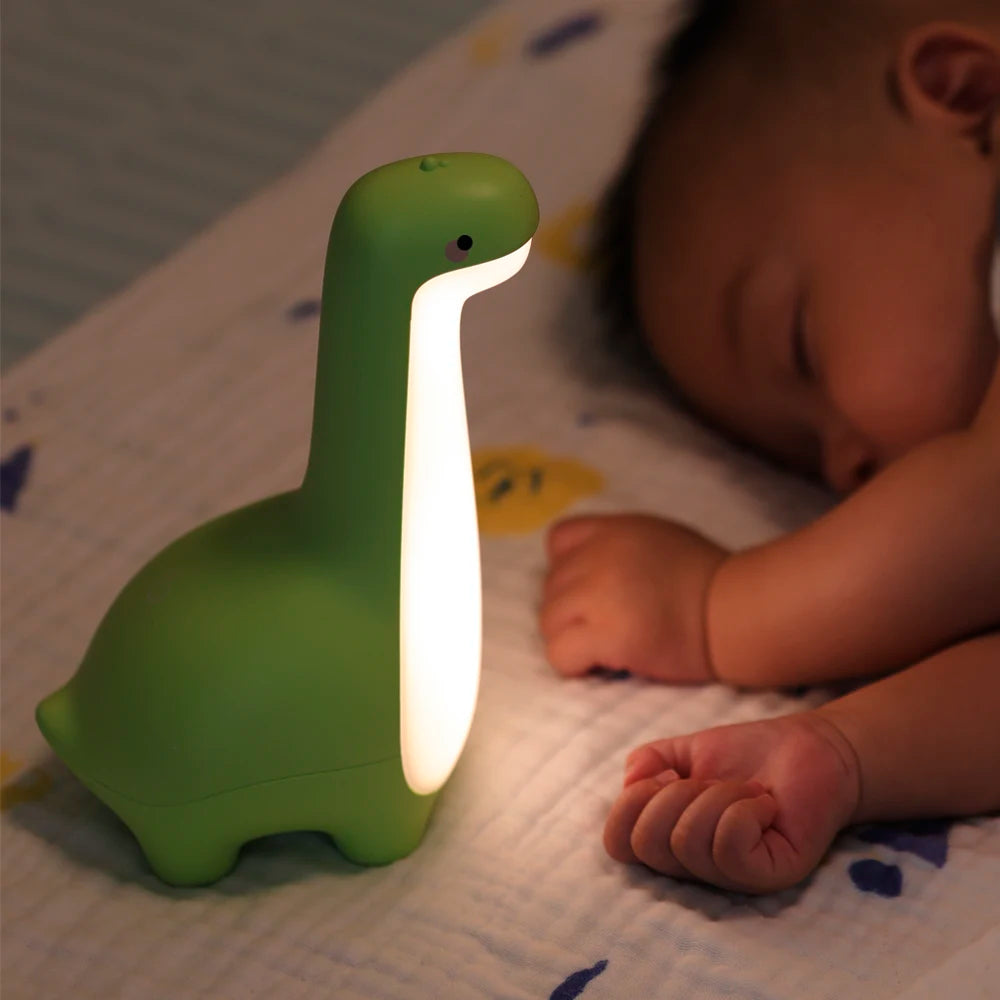 Green dinosaur-shaped kawaii night light next to a sleeping baby