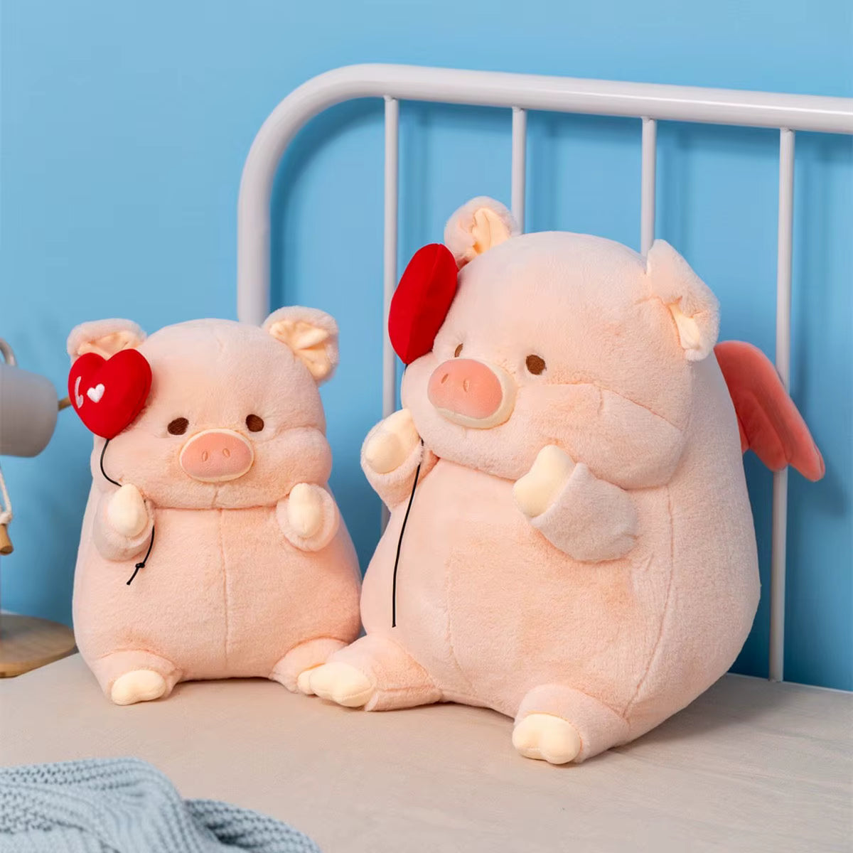 Two plush pig toys with red hearts on a bed against a blue wall