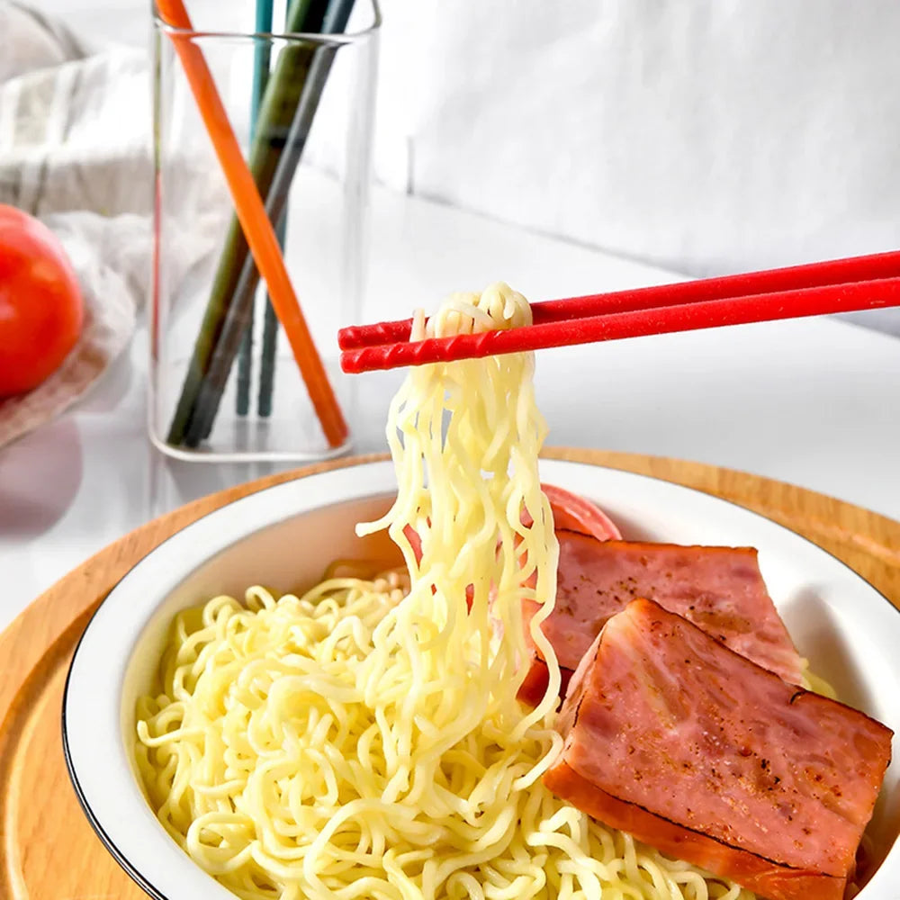 Noodles with ham being lifted with red kawaii chopsticks on a white plate.