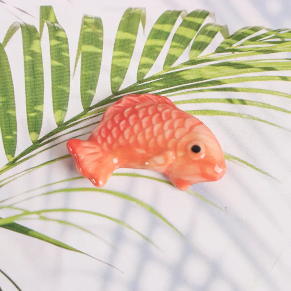 Coral-colored fish-shaped kawaii chopstick holders on a leafy background