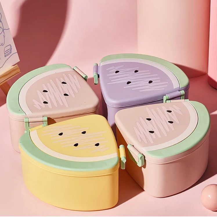 Set of four colorful watermelon-shaped kawaii bento boxes on a pink background