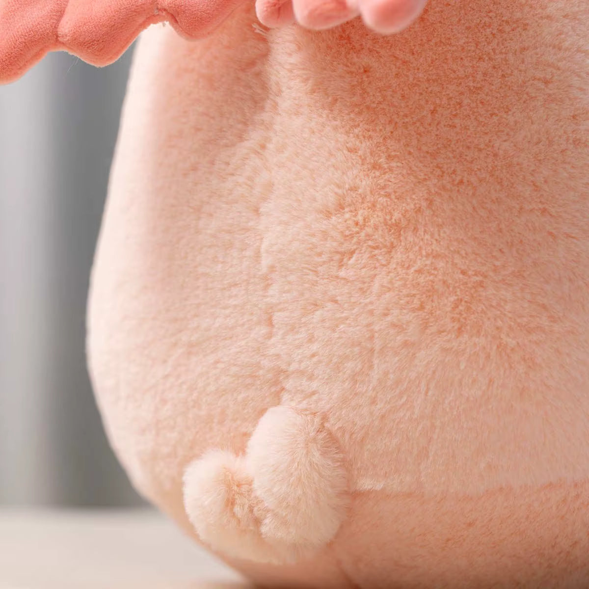 Close-up of a soft peach-pink plush toy with fuzzy texture and a small rounded tail detail.