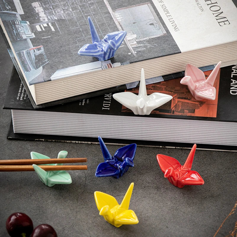 Colorful origami crane-shaped kawaii chopstick holders on a surface with books in the background.