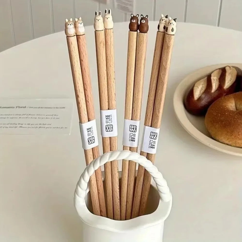 Wooden kawaii chopsticks with animal-shaped tips in a white holder on a table with bread in the background.