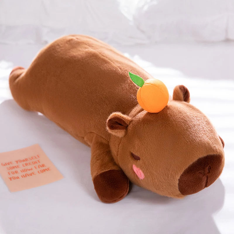 Brown kawaii plush toy resembling a bear with an orange on its head, lying on a white surface.