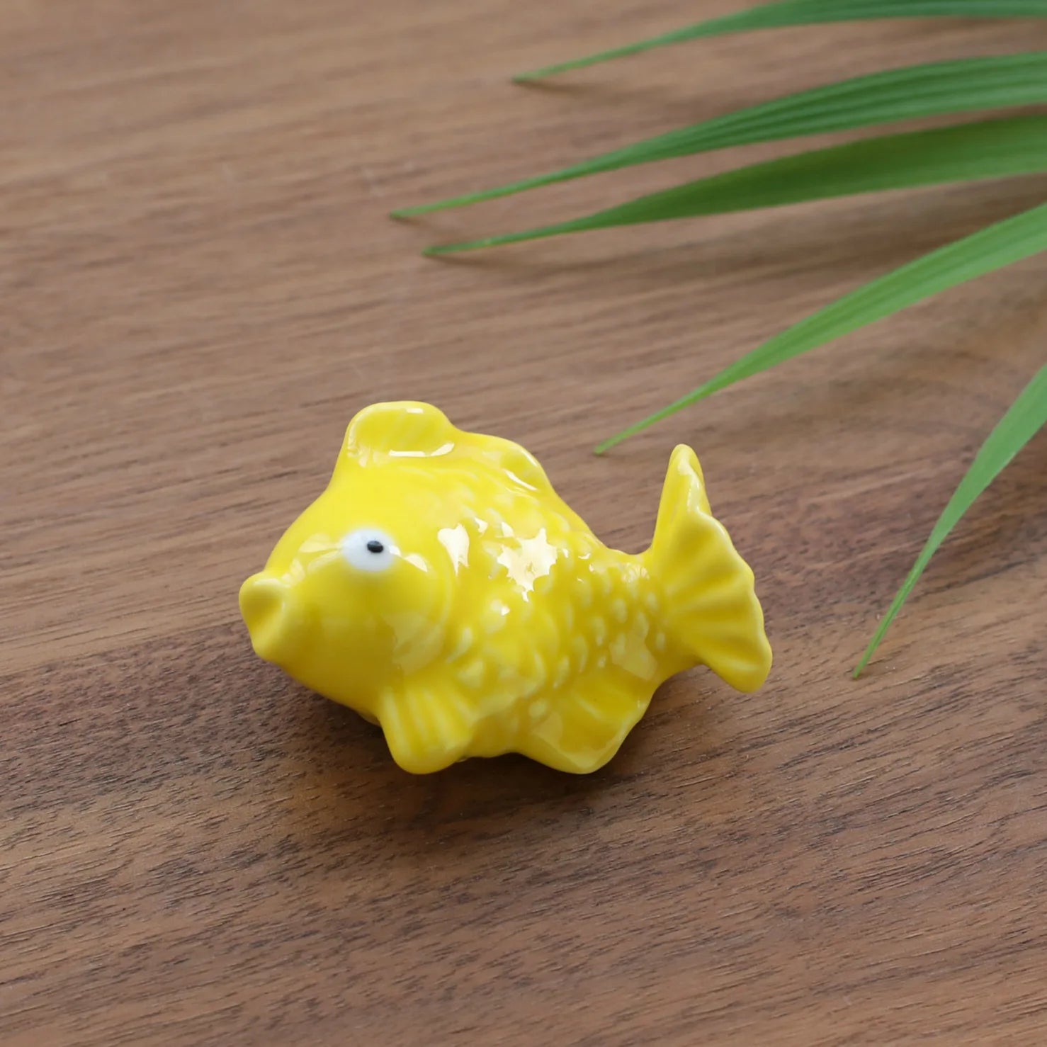 Yellow fish-shaped kawaii chopstick holders on a wooden surface with grass