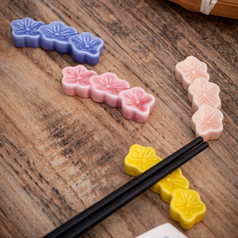 Colorful flower-shaped kawaii chopstick holders on a wooden surface with black chopsticks.