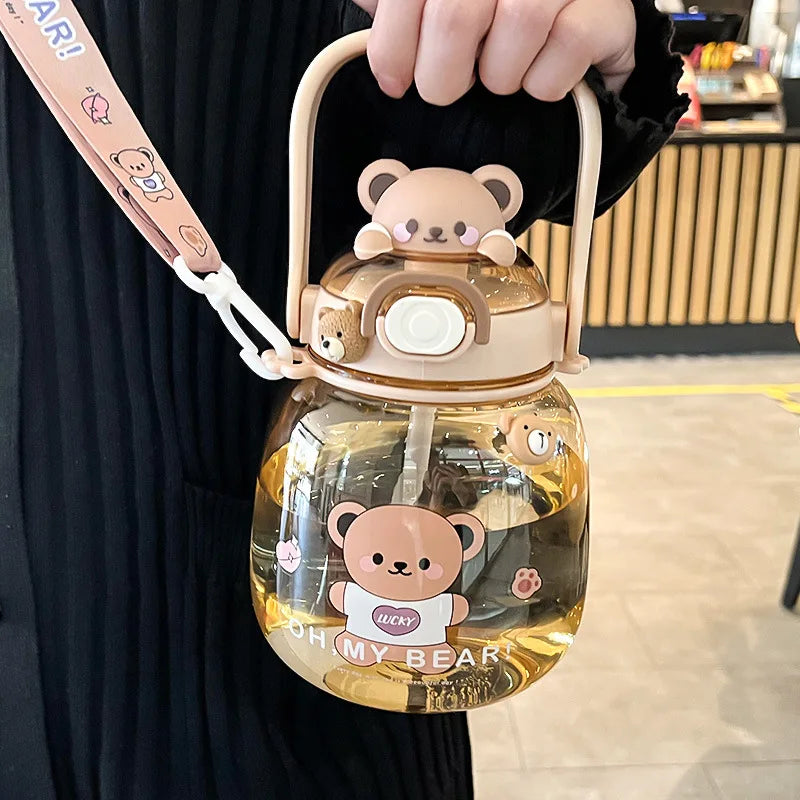 Clear kawaii water bottle with bear design and pink strap held by a person indoors.