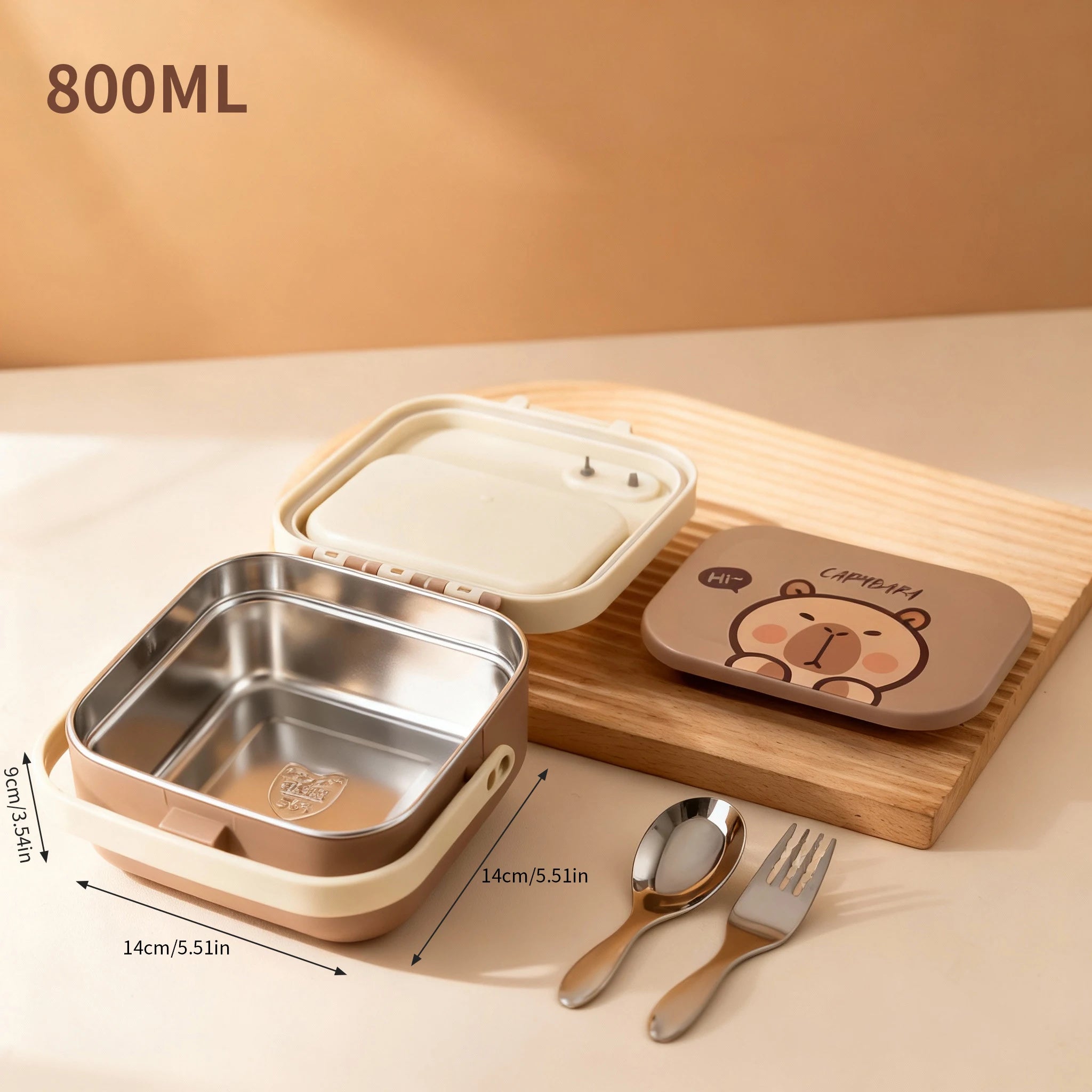 Stainless steel kawaii lunch box with cartoon lid, spoon, and fork on a wooden board.