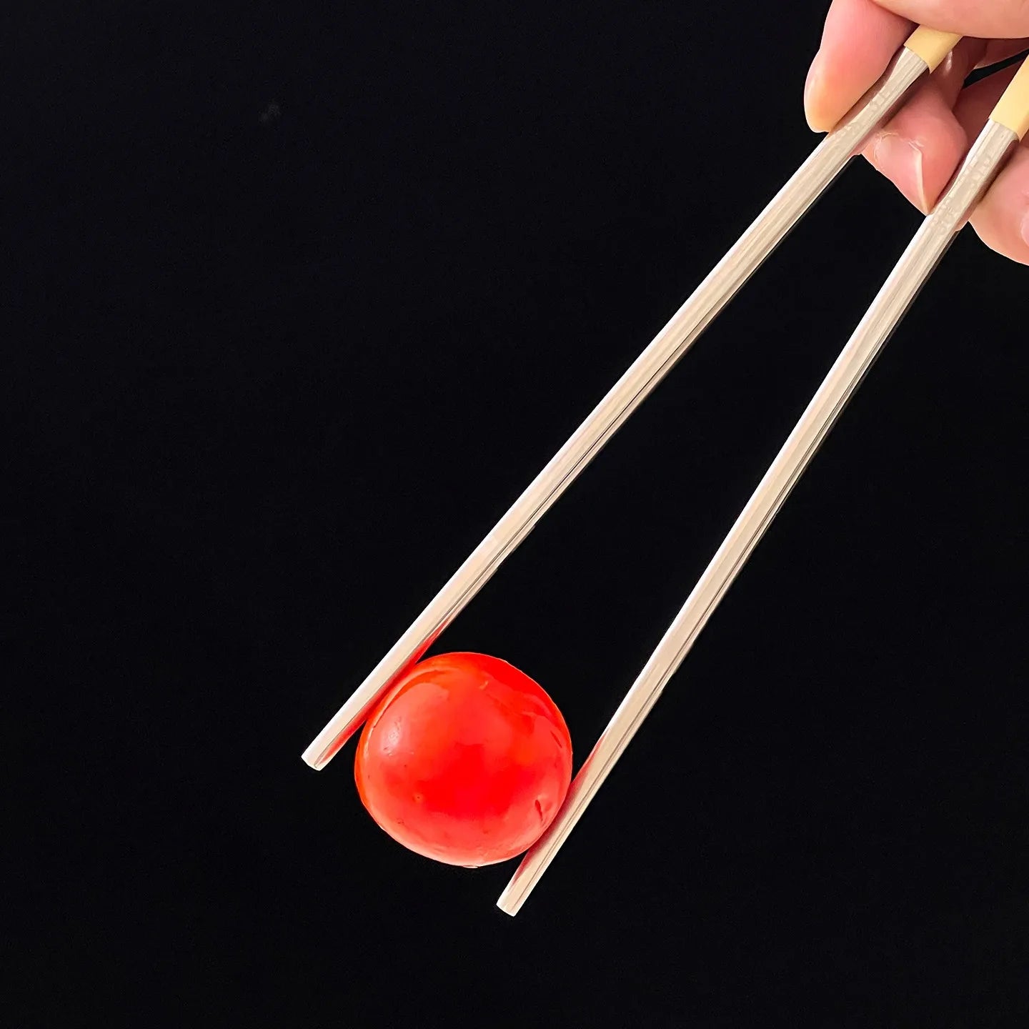 Kawaii chopsticks holding a red ball against a black background