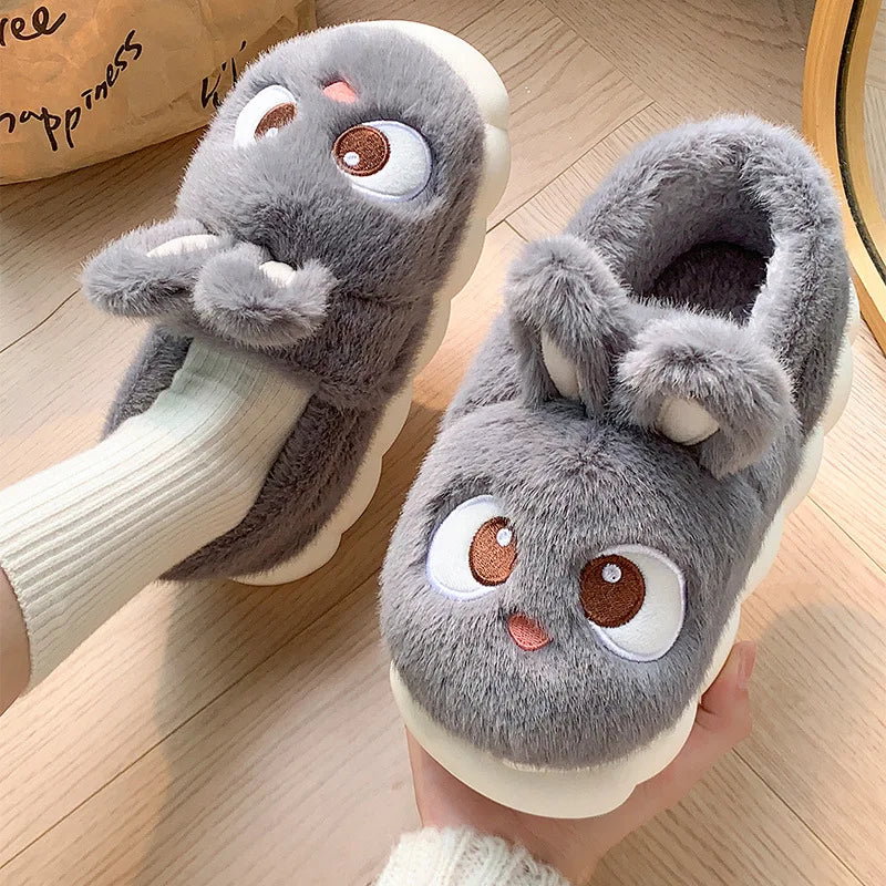 Gray plush kawaii slippers with cartoon face design worn indoors on a wooden floor.