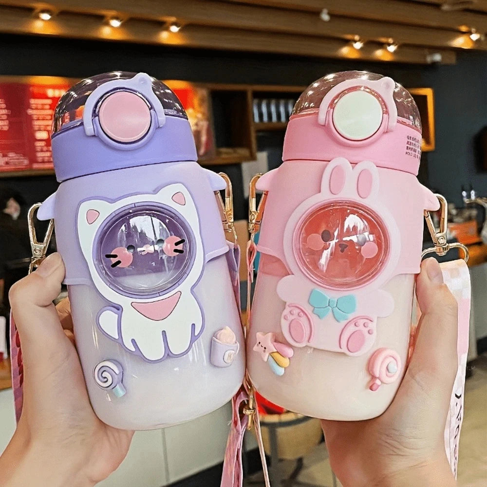 Two cartoon-style kawaii water bottles held in hands with a blurred indoor background.