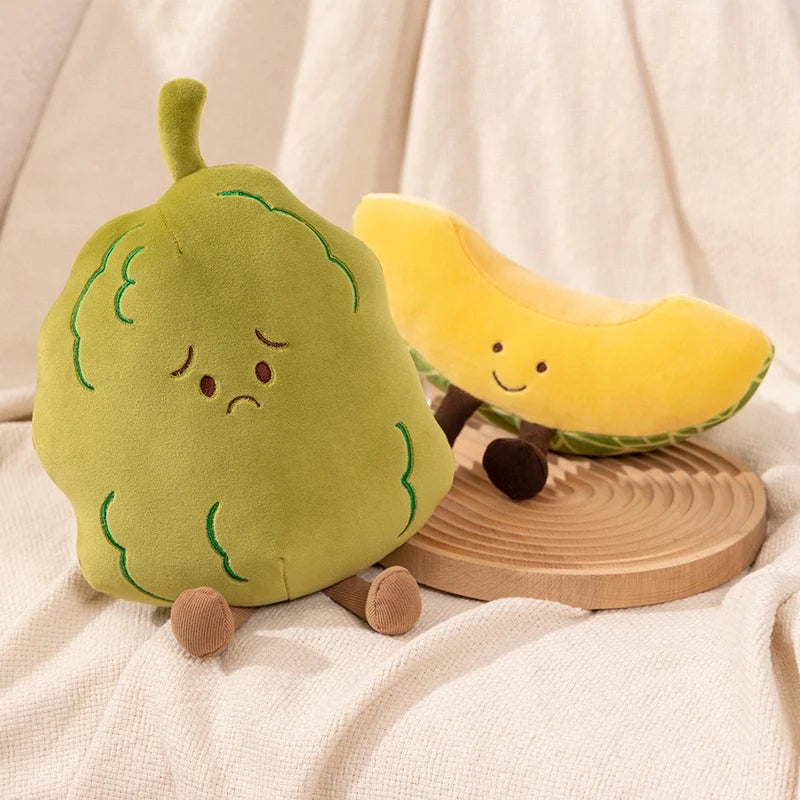 Two cute plush fruit toys, a sad green pear and a smiling yellow banana, styled on a cream fabric background with a small wooden slice stand.