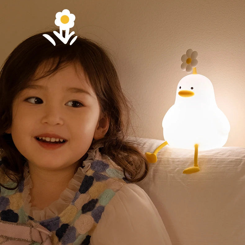 Child smiling next to a cute duck-shaped kawaii night light with a flower on its head.