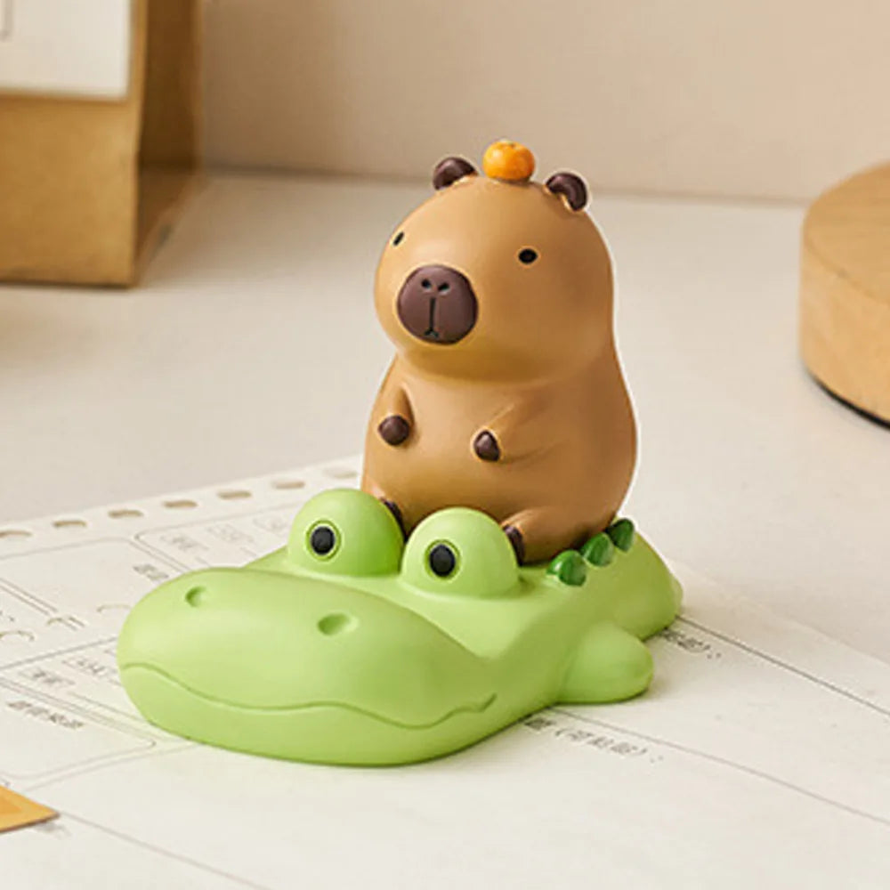 Kawaii phone holder of a brown animal on top of a green crocodile toy on a light surface.