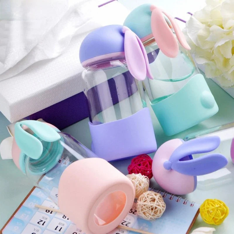 Colorful bunny-shaped kawaii water bottles on a light surface with flowers in the background