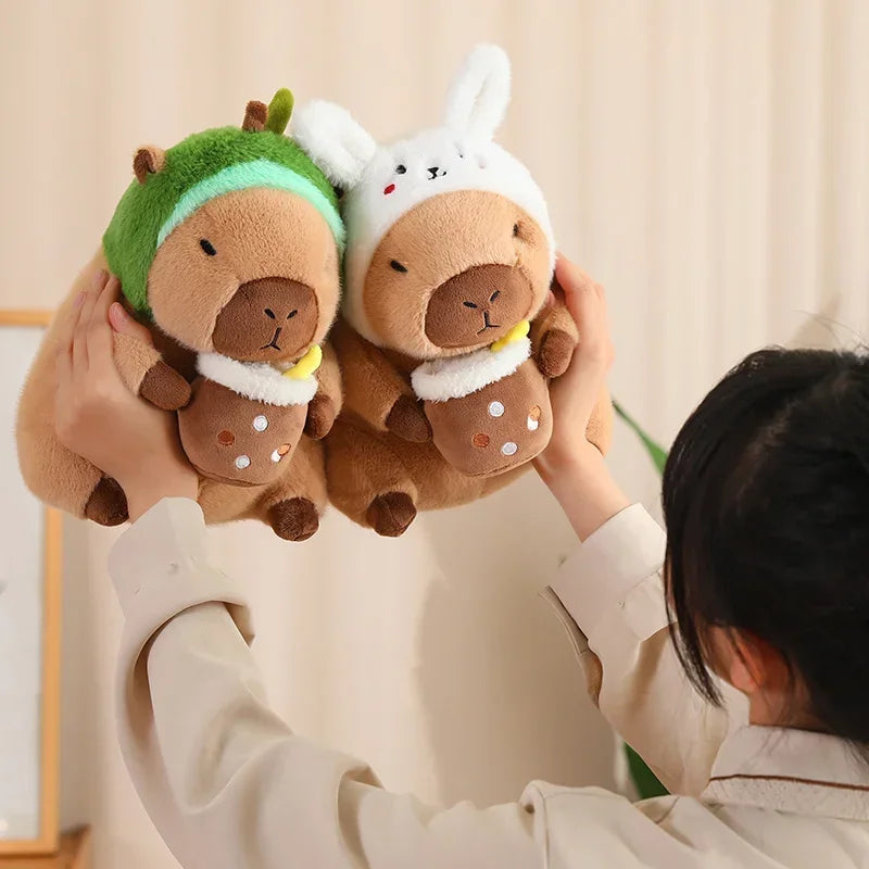 Person holding two kawaii plush toys resembling animals with hats against a neutral background