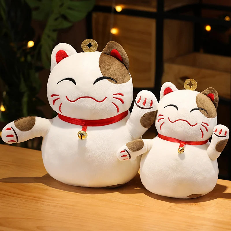Two kawaii plush maneki-neko figures on a wooden surface with a blurred background