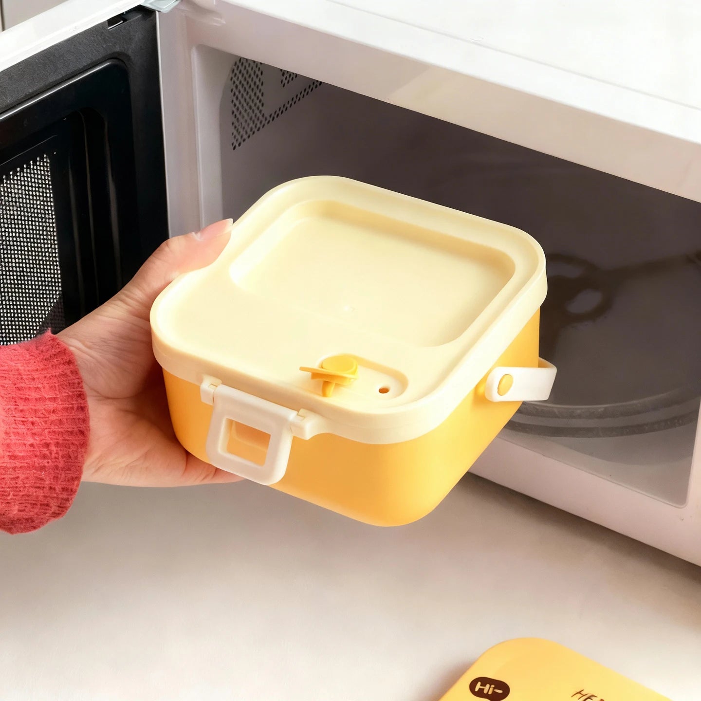 Yellow and white kawaii food container held in front of a microwave
