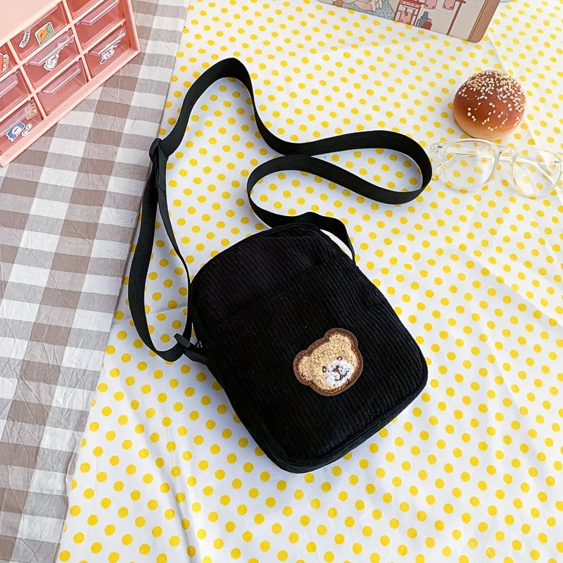 Black crossbody bag with a bear design on a yellow polka dot surface