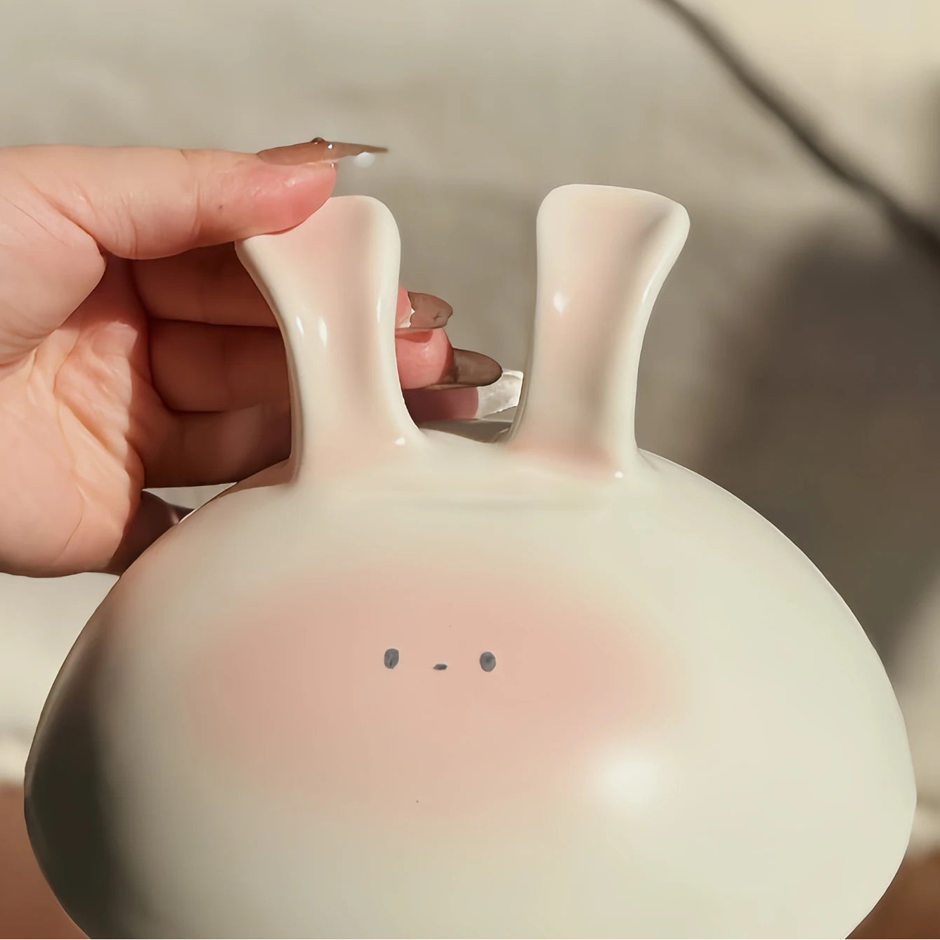 Hand holding a white ceramic kawaii bowl with a face design against a blurred background