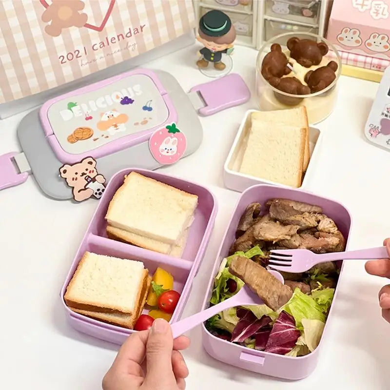 Kawaii bento box with compartments containing sandwiches and salad, with a calendar and small figurines in the background.