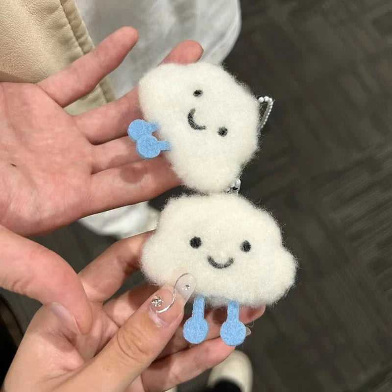 Two kawaii fluffy cloud-shaped keychains with smiling faces and blue feet held by a person.