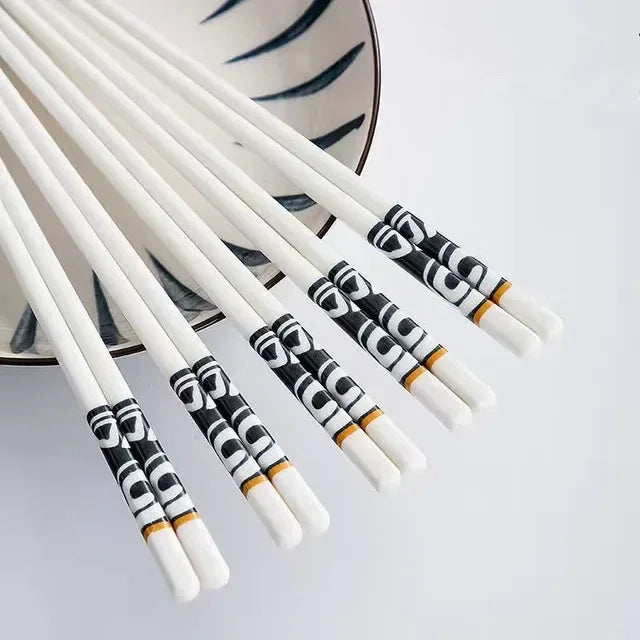 Set of white kawaii chopsticks with black and gold patterns on a light gray background