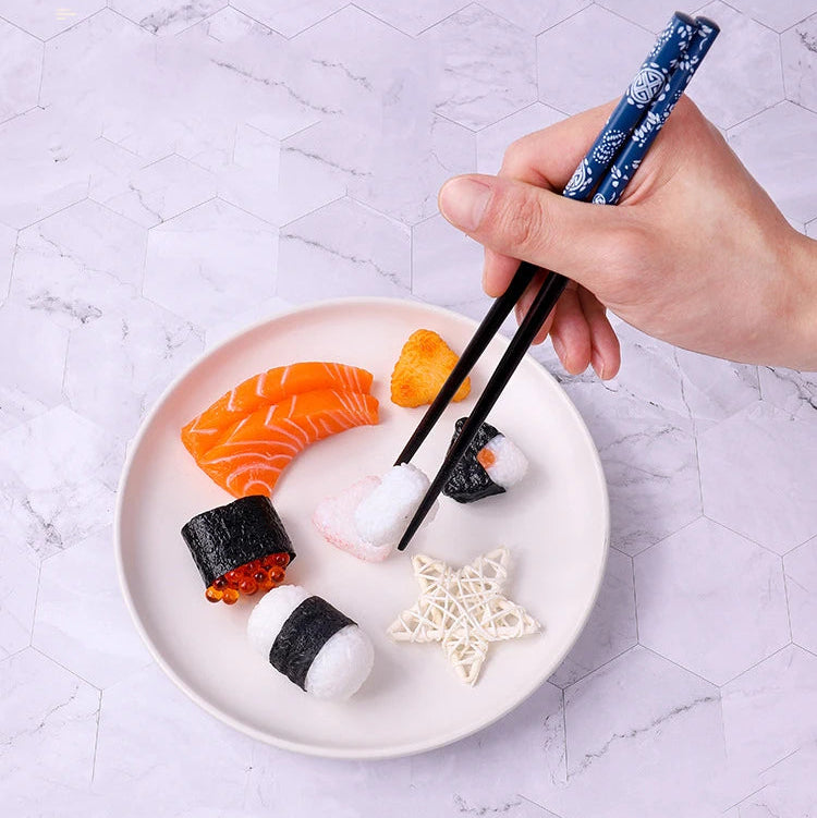 Hand using kawaii chopsticks to pick up sushi from a plate on a light gray marble surface.