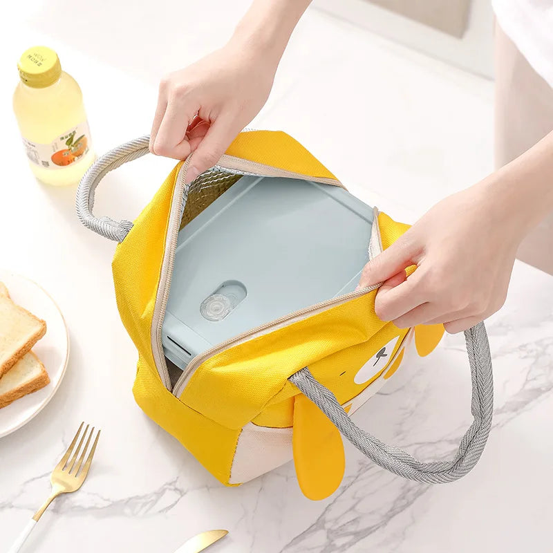 Yellow kawaii lunch bag with a compartment on a marble surface with a plate of food.