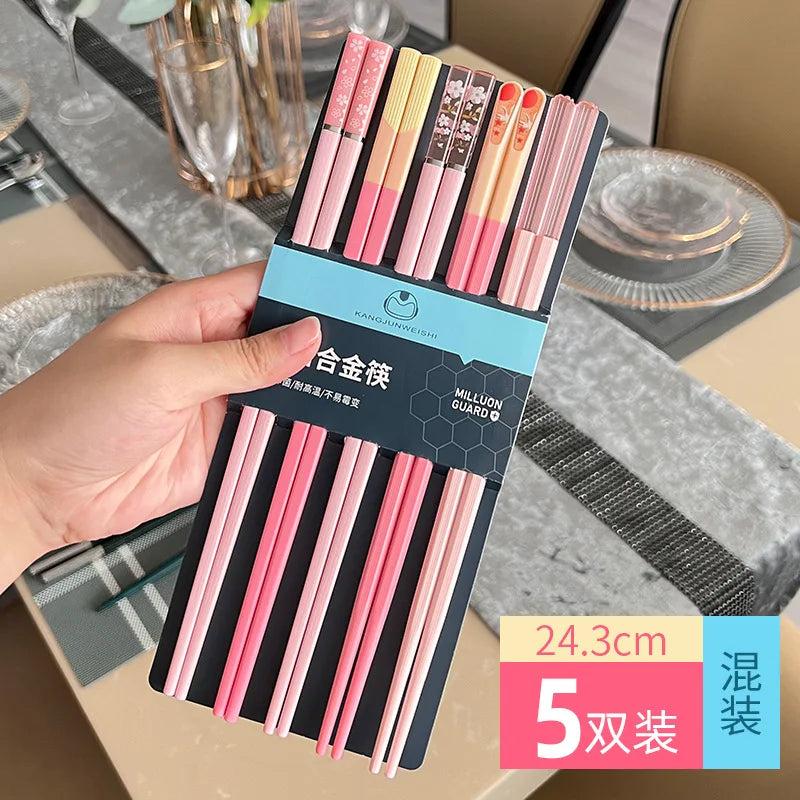 Packaged pink and black kawaii chopsticks held by a hand with a dining table setting in the background.
