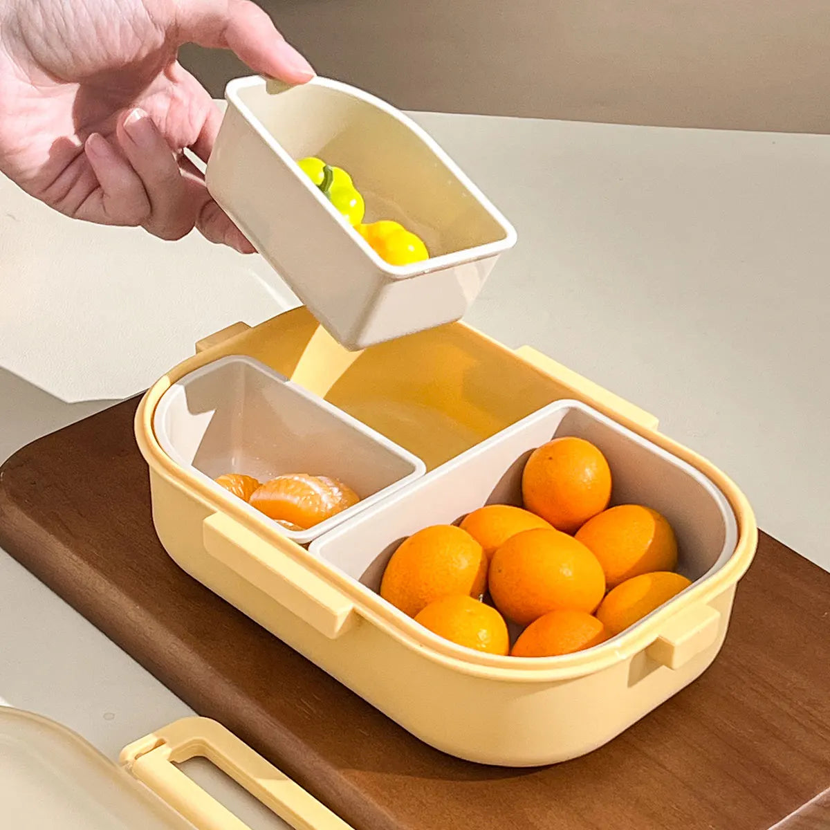 Yellow kawaii bento box with compartments being used to store oranges and lemons on a wooden surface.