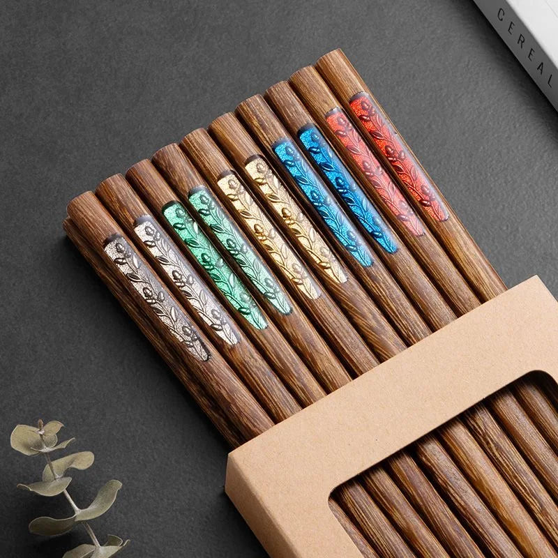 Set of wooden kawaii chopsticks with colored ends and engraved designs in a cardboard holder on a dark surface.