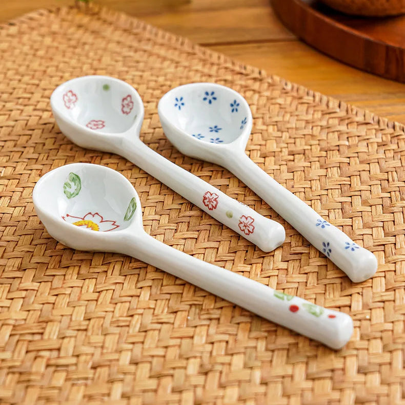 Three white ceramic kawaii spoons with floral patterns on a woven mat