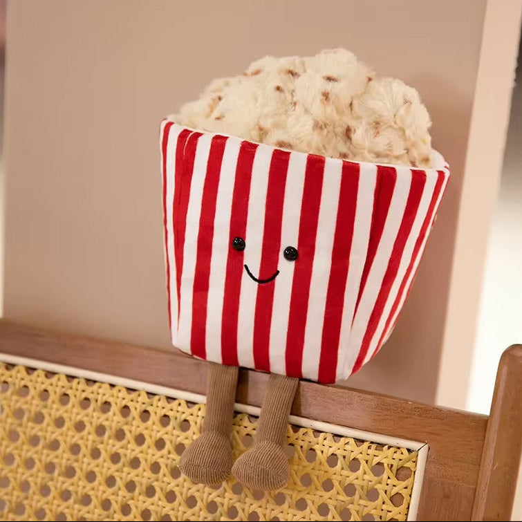 Kawaii plush toy resembling a popcorn bucket with legs and a smiling face on a wooden surface.