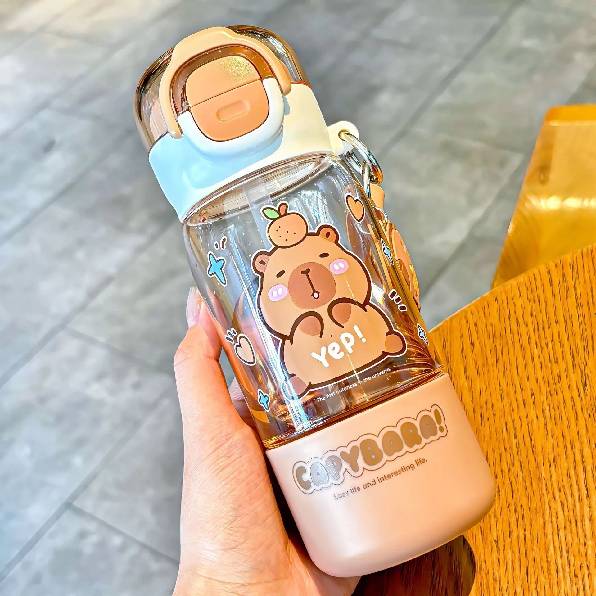 Clear kawaii water bottle with cartoon bear design held by a hand on a wooden surface.