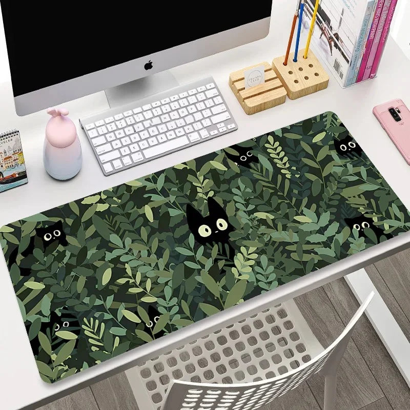 Desk setup with a green desk mat featuring black cat designs, keyboard, and computer monitor.