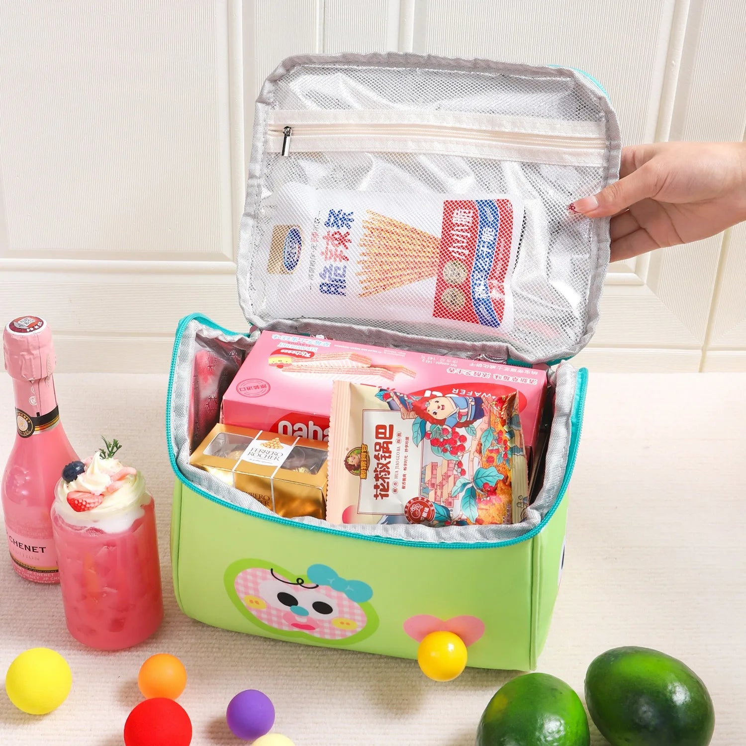 Green kawaii lunch bag with snacks and drinks on a light wooden surface