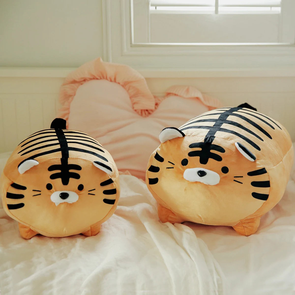 Two tiger-shaped kawaii cushions on a bed with a neutral background