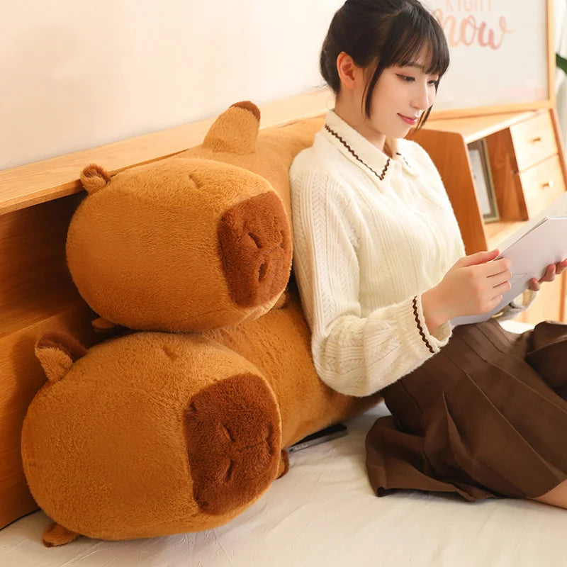 Woman sitting on a couch next to a large brown kawaii plush toy, holding a tablet.