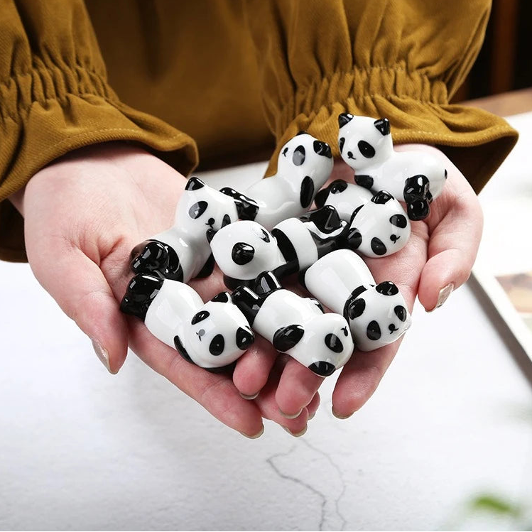 Hands holding panda-shaped kawaii chopstick holders with a blurred background