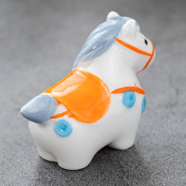 White ceramic horse kawaii chopstick holders with orange and blue accents on a gray background