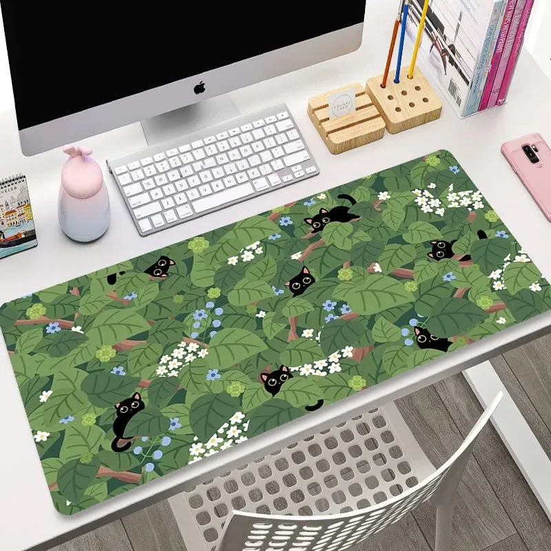 Desk setup with a green desk mat featuring black cat designs, keyboard, and office items.