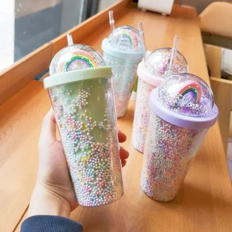 Set of glittery kawaii tumblers with rainbow designs on a wooden table.