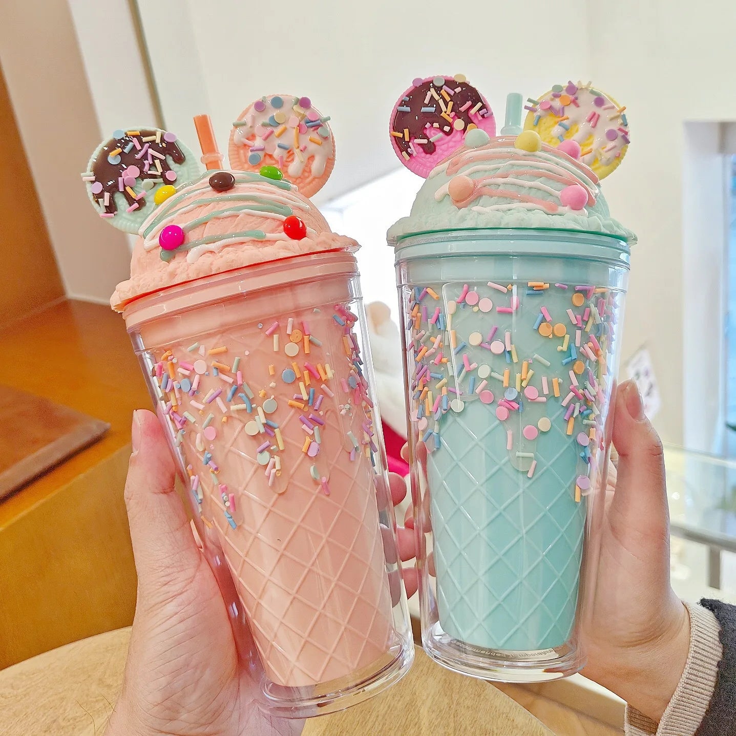 Two colorful kawaii tumbler cups with ice cream cone design held by a person.