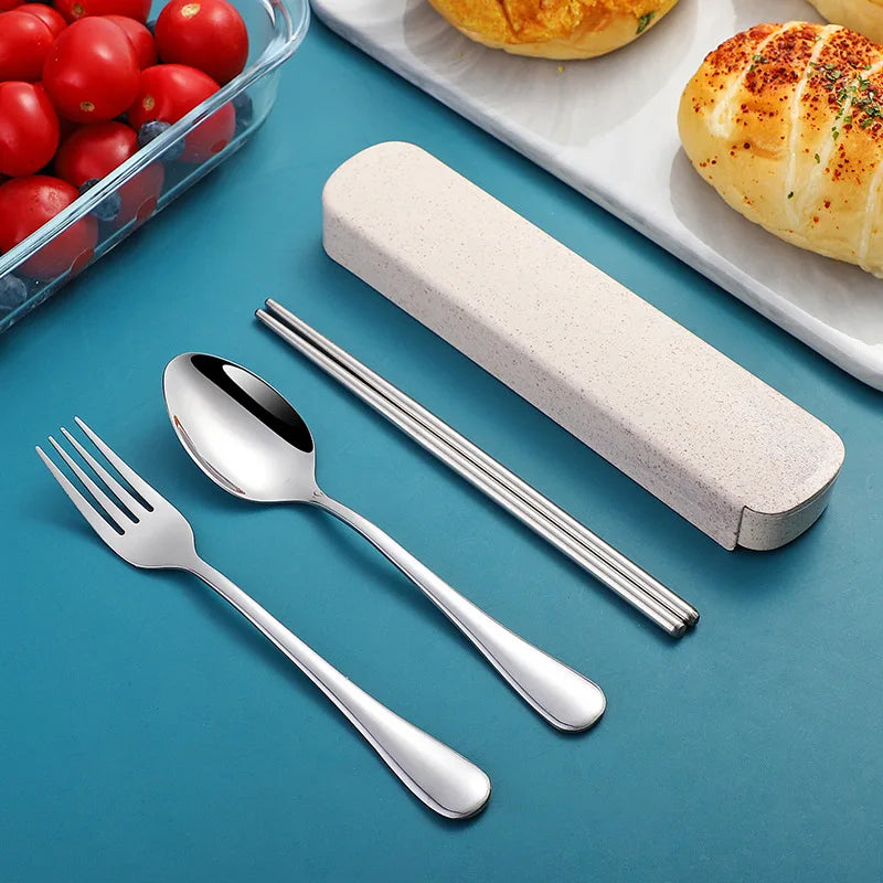 Stainless steel kawaii utensils set with case on a blue surface, next to tomatoes and bread.