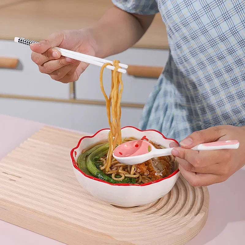 Person eating ramen with a decorative bowl and kawaii spoon on a wooden table.