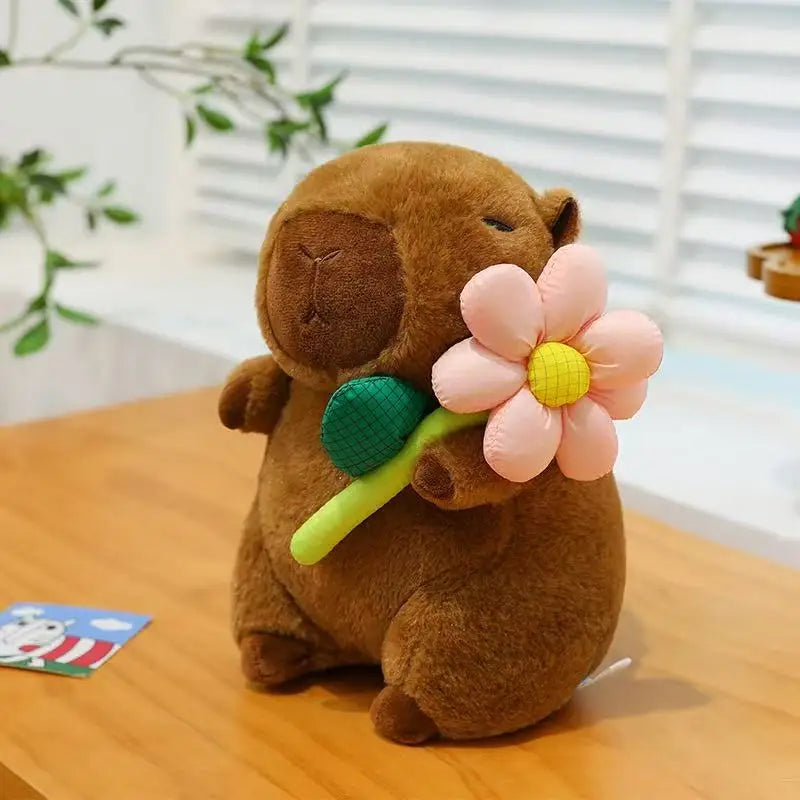 Brown kawaii plush toy holding a pink flower on a wooden surface with a blurred background