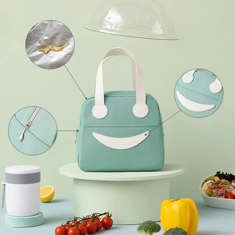 Green kawaii lunch bag with smiley face design on a light green background with food items around.